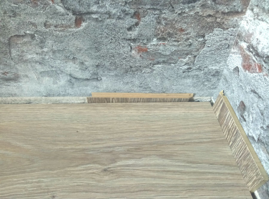Зафіксуйте відступ за допомогою розпірок або непотрібних шматочків ламінату. Зазор між покриттям підлоги і стінами повинен бути 8-12 мм.