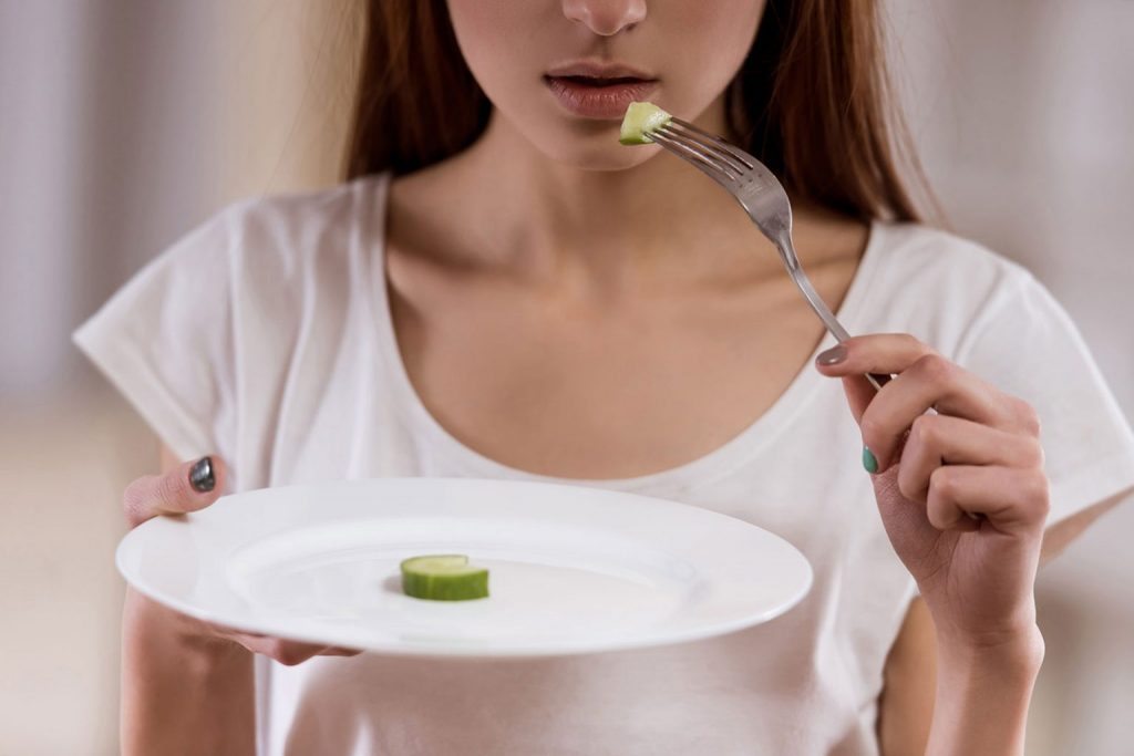 Девушка ест из тарелки, на которой один кружок огурца
